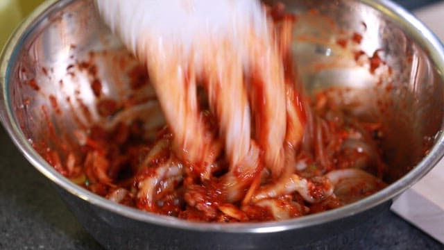 Mixing fresh webfoot octopus and gochujang seasoning in a metal bowl