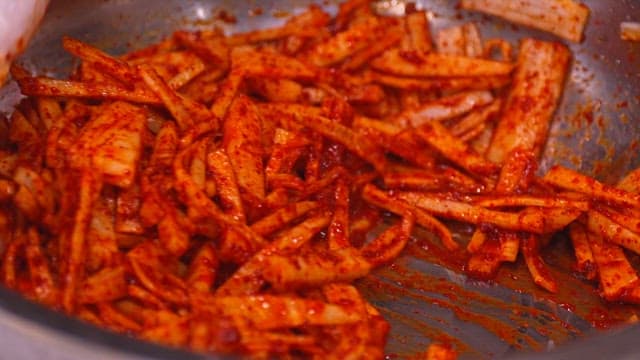 Make the julienne Korean radish salad by mixing the red pepper powder in a large bowl