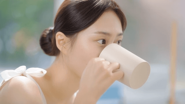 Woman cleaning her mouth with water from a cup in front of a bathroom mirror
