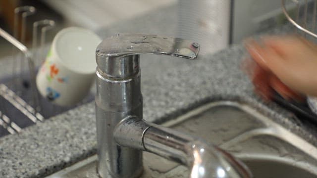 Washing dishes in the kitchen sink with running water