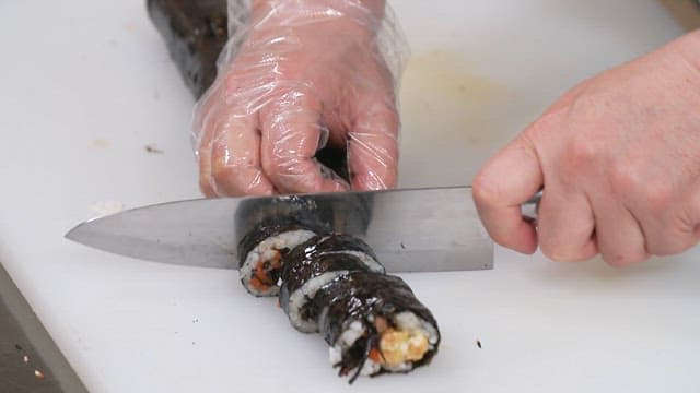 Hand cutting kimbap on a cutting board
