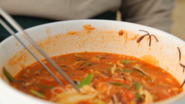 Picking up cold raw fish soup with noodles using chopsticks
