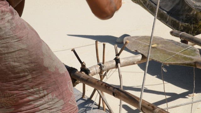 Two men constructing a traditional wooden frame on a sandy beach
