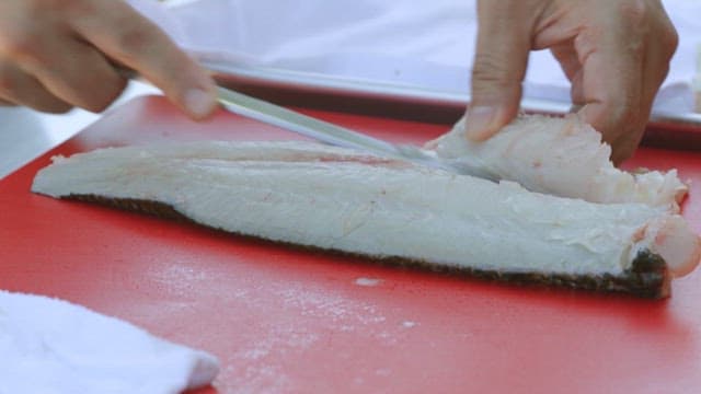 Fish being prepared with a knife on a red cutting board