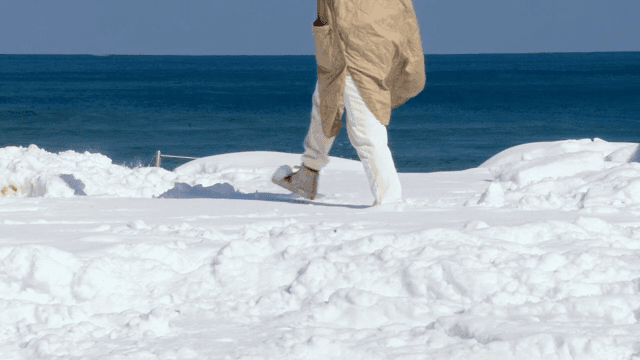Person walking on a snowy beach by the sea