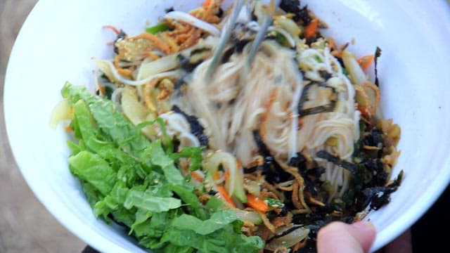 Mixing fresh vegetables, anchovies, and noodles in a bowl
