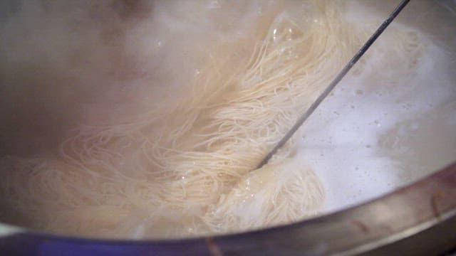 Wheat noodles boiling in a pot with steam