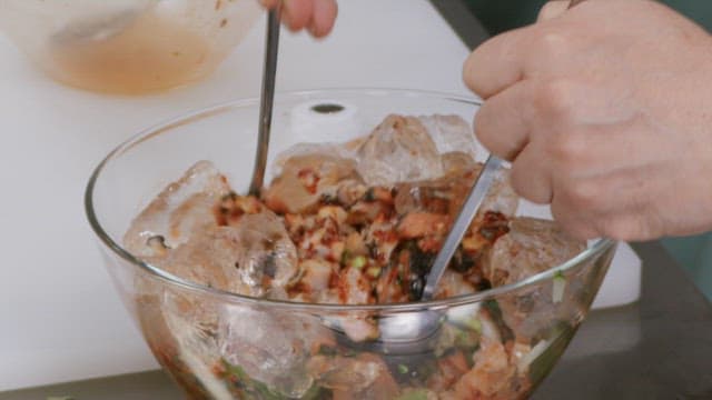 Hands mixing a fresh vegetable and seafood dish in a glass bowl with ice