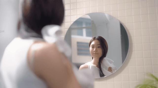 Woman drying her hair with a towel in front of a bathroom mirror