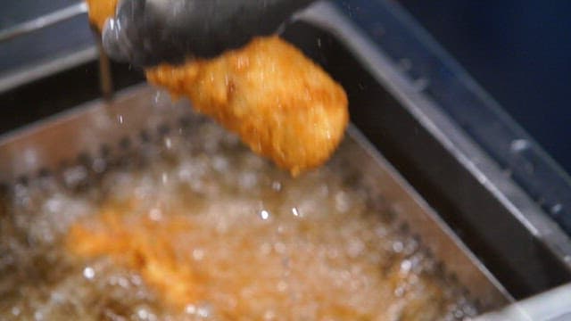 Crispy pork cutlet fried in deep fryer being lifted with tongs