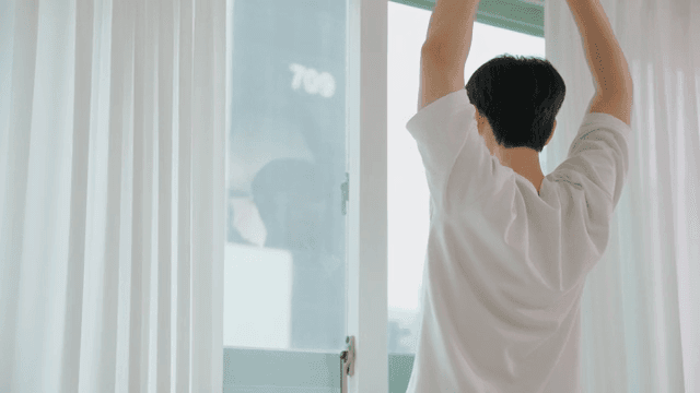 Man opening white curtains and stretching