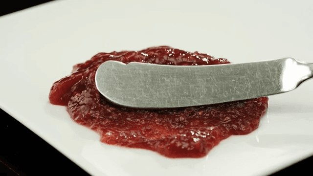 Spreading strawberry jam with a butter knife on a white plate