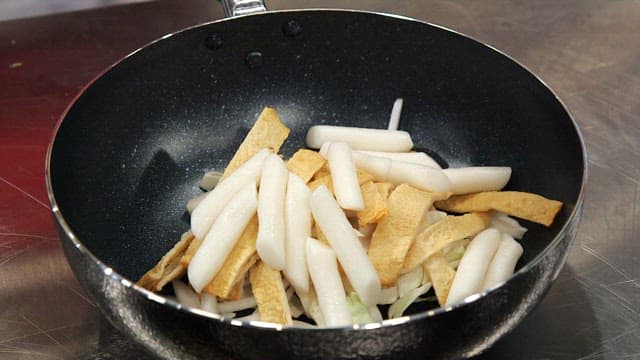 Preparing tteokbokki by adding gochujang to the pan with rice cakes and fish cake
