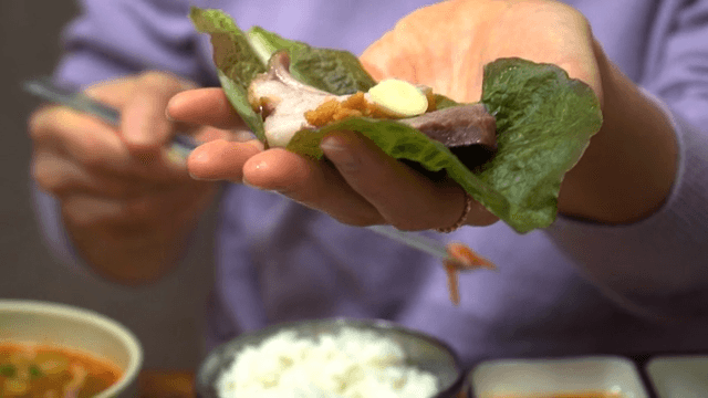 Making a wrap by putting boiled pork, garlic, pepper, and rice on lettuce