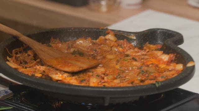 Cooking kimchi fried rice in a hot pan on a stove with wooden spatula
