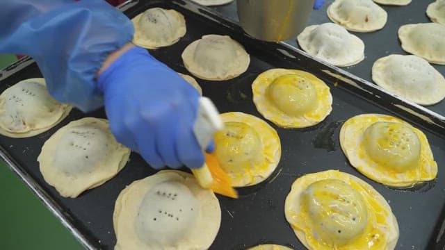 Bread dough being brushed with egg wash in a bakery kitchen