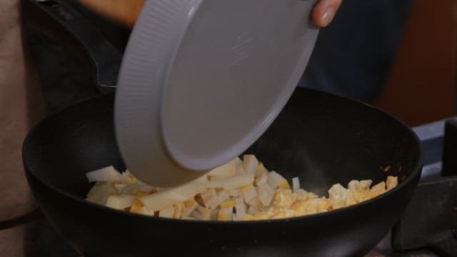 Adding bamboo shoots to a frying pan with fried eggs