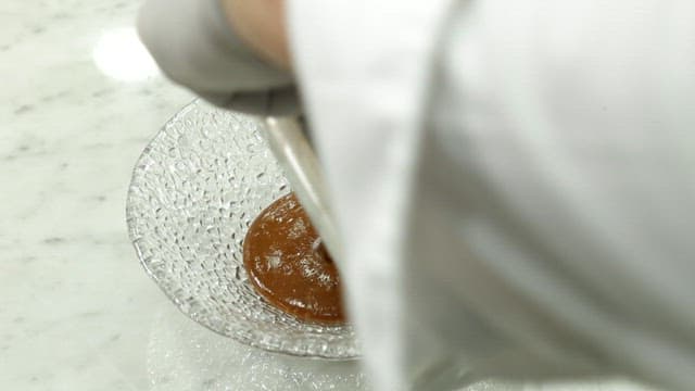 Person preparing a sauce made with red bean in a glass bowl
