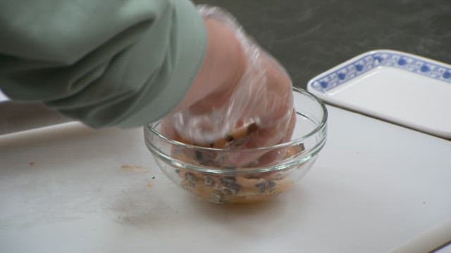 Hands wearing plastic gloves preparing abalone in a glass bowl