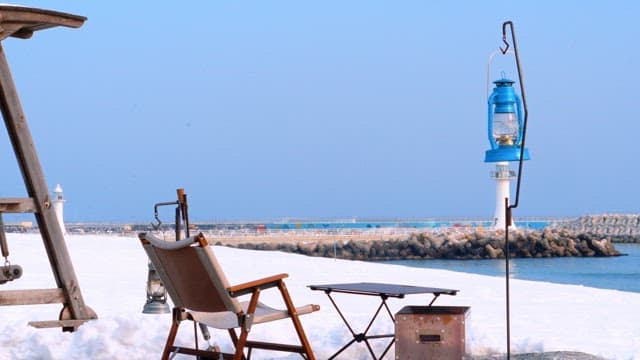 Camping chairs and lanterns on a snowy beach with a view of the breakwater