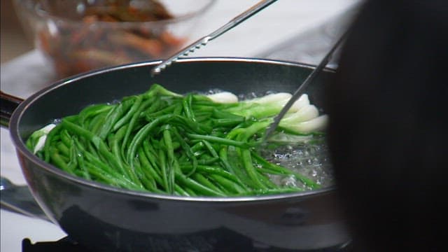 Green onions lightly blanched in boiling water being placed in a metal bowl