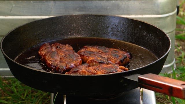 Grilling steaks on a hot frying pan, turning with tongs