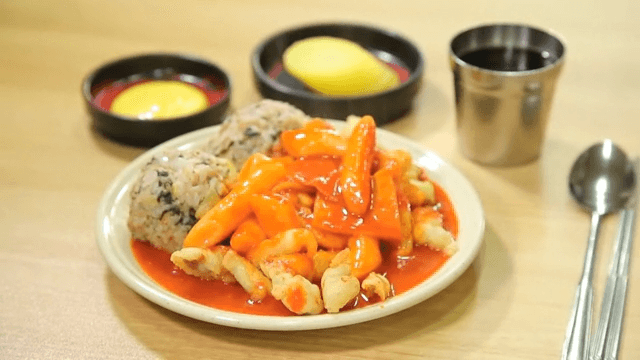 Table with plate of spicy tteokbokki and rice balls and pickled radish