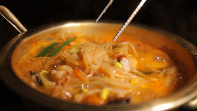 Picking up spicy bean sprout kalguksu noodles boiling in a nickel-silver pot with chopsticks