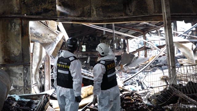 Police investigators inspect a burnt building wreckage.