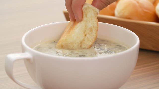 Hand dipping bread in bowl of creamy soup