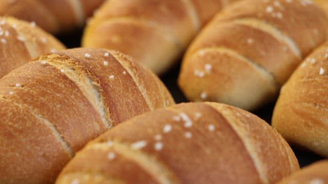 Freshly baked salted butter rolls being picked up with tongs