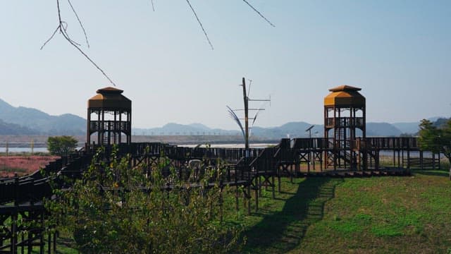 Scenic viewpoint with a yellow wooden tower and a modern sculpture, set by a river in a green park