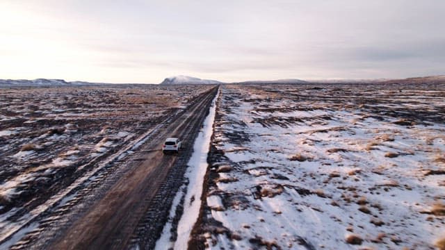 Car driving on a snowy road in open fields