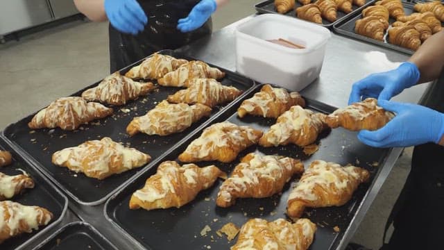 Bakers stuffing sausages into freshly baked croissants in a bakery kitchen