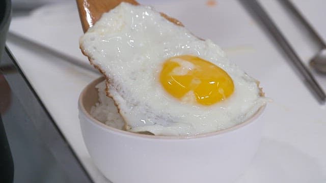 Fried egg and rice being plated on a wooden ladle