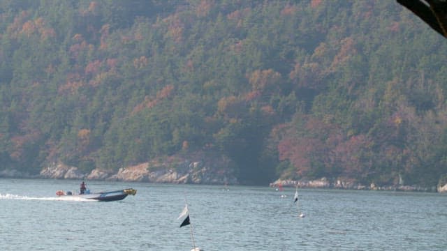 Boat speeding on a calm sea with forested hills