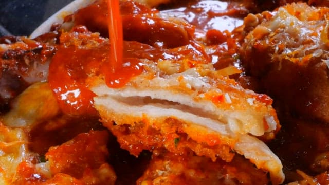 Red and spicy sauce being poured over a layered dish