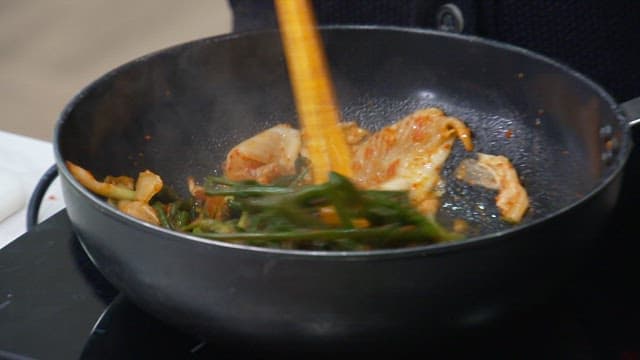 Stir-frying cabbage kimchi and green onion kimchi in oil using chopsticks