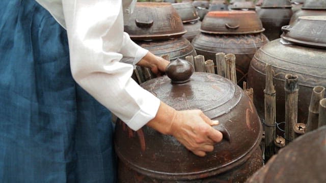 Person opening a traditional Korean jar