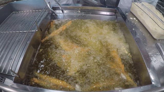 Cooking skewered sand eels from a deep fryer full of oil in a commercial kitchen
