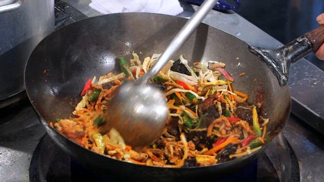 Stir-frying vegetables and meat with spicy sauce in a wok