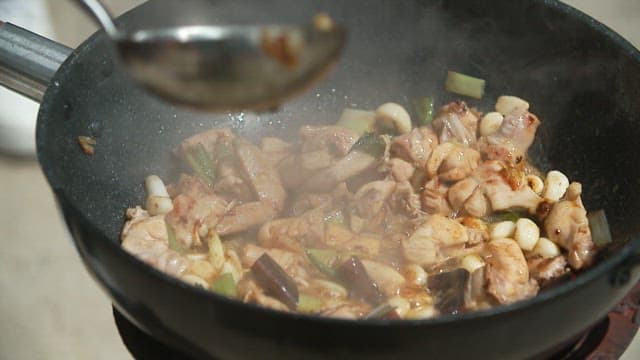 Sauce and meat being stir-fried over high heat in a large wok