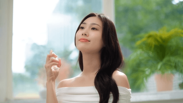 Woman spraying perfume indoors with a smile