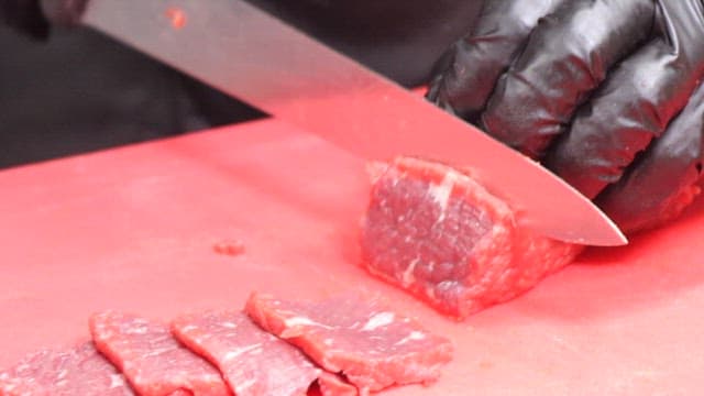 Cutting Raw Meat on a Cutting Board Wearing Gloves