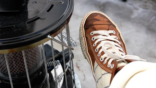 Person drying shoes near a portable heater outdoors