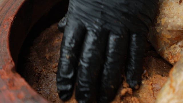 Hand in a black glove mixing traditional fermented paste in a jar