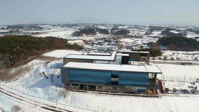 Large building in a snowy landscape with surrounding forests and small town