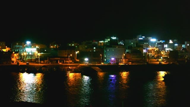 Nighttime view of a coastal city with bright lights reflecting on the water