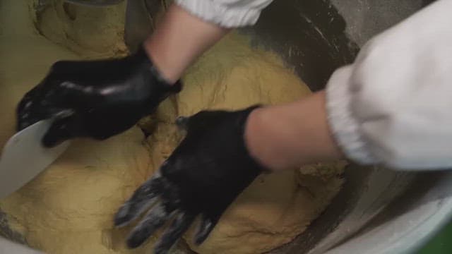 Person kneading dough in a large mixing bowl using black gloves