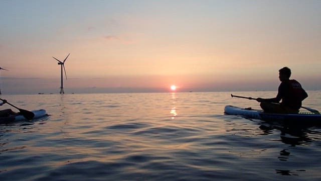Paddlers at Sea During Sunset with Wind Turbines